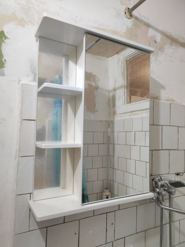 Изображение ванной комнаты с установленным зеркальным шкафом, плиткой на стенах и смесителем. Стены подготовлены для дальнейших работ, виден небольшой участок с неокрашенной поверхностью.