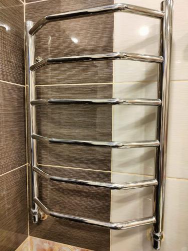 На стене ванной комнаты закреплён новый хромированный полотенцесушитель. Подключены трубы, обеспечивающие циркуляцию воды. Устройство функционирует, готово к использованию.