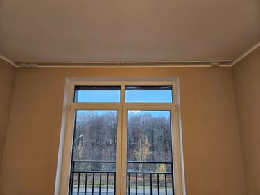 Закреплен карниз над окном, ровно выровнен, надежно зафиксирован на стене, обеспечивая устойчивость и готовность к использованию. Работа выполнена аккуратно, без видимых дефектов.