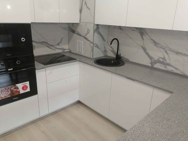Установлена кухонная поверхность из искусственного камня, идеально подогнанная по размерам, с вырезами для мойки и варочной панели, надежно закрепленная и герметично обработанная.