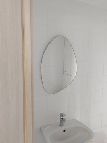 На стене ванной комнаты установлено овальное зеркало. Закреплено надежно, ровно, без видимых крепежей. Поверхность плитки осталась целой, без повреждений.