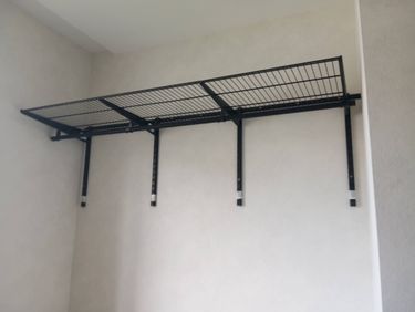 Установлена металлическая полка на стену с помощью крепежных элементов. Конструкция надежно закреплена и выровнена по уровню, обеспечивая устойчивость и безопасность.