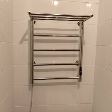 На стене ванной комнаты закреплен электрический прибор для сушки полотенец. Подключен к сети, проверена работоспособность. Устройство надежно зафиксировано, кабель аккуратно уложен.