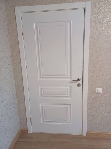 На белой двери аккуратно установлен замок с ручкой. Работа завершена: вырезано отверстие, вставлен механизм, закреплены элементы. Все выполнено точно и надежно.