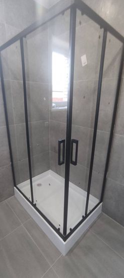 Установлена стеклянная конструкция с черными рамами на поддон, закреплены дверцы, герметизация швов, проверена устойчивость и герметичность, завершена отделка плиткой.
