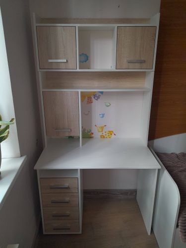 Собран компактный шкаф с полками и ящиками, установлен в комнате. Конструкция выполнена из светлого дерева, оснащена ручками. Все элементы надежно закреплены, обеспечивая устойчивость.