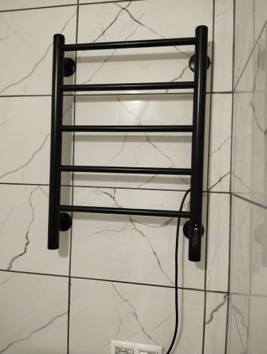 Установлен черный электрический прибор на стену с плиткой. Подключен к розетке, закреплен надежно. Проведена проверка работы устройства, все функционирует корректно.