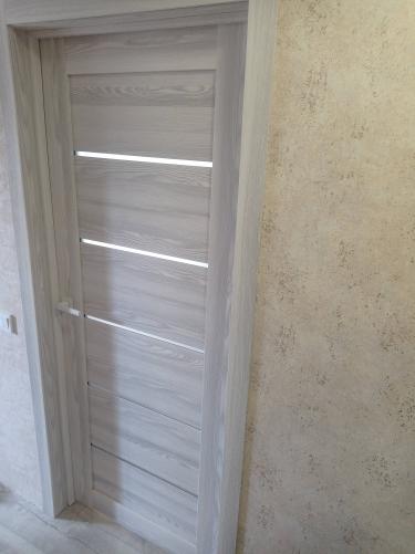 Установлена светлая дверь с горизонтальными вставками, аккуратно закреплена в проеме, добавлена ручка. Завершены все монтажные работы, обеспечена плавная работа конструкции.