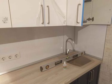 Установлены шкафы, закреплены ручки, смонтирована столешница, врезана мойка, подключен смеситель, выровнены поверхности, установлены розетки, завершена отделка стен.