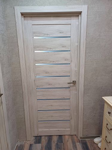 Установлена светлая межкомнатная дверь с горизонтальными вставками и металлической ручкой. Дверная коробка закреплена, полотно ровно висит, зазоры отсутствуют.