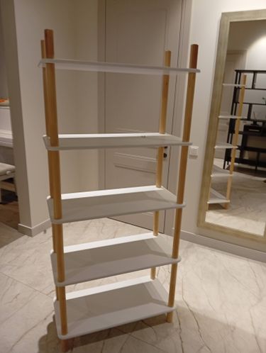 Собран новый стеллаж с пятью белыми полками и деревянными стойками. Конструкция устойчива и готова к использованию. Установлена в интерьере с современным дизайном.