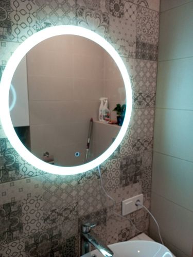 Установлено круглое зеркало с подсветкой на кафельной стене в ванной комнате, подключено к электросети, обеспечена надежная фиксация и ровное расположение над раковиной.