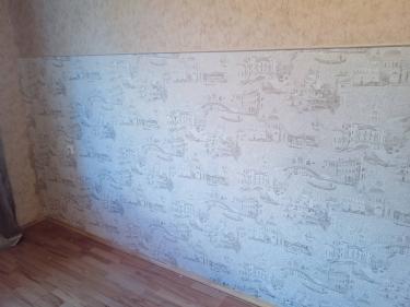 На стенах завершена работа: наклеены обои с городским узором. Поверхность ровная, стыки аккуратные, рисунок совпадает. Пол и плинтус чистые, без следов клея.