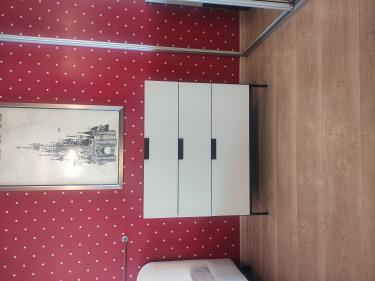 Собран белый комод с тремя ящиками, установлен на деревянный пол у стены с красными обоями в звёздочку, рядом зеркало и картина.