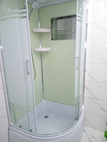 Установлена современная душевая конструкция с прозрачными дверцами, оборудована лейкой и полками. Стены облицованы плиткой, обеспечивающей водонепроницаемость и стильный вид.