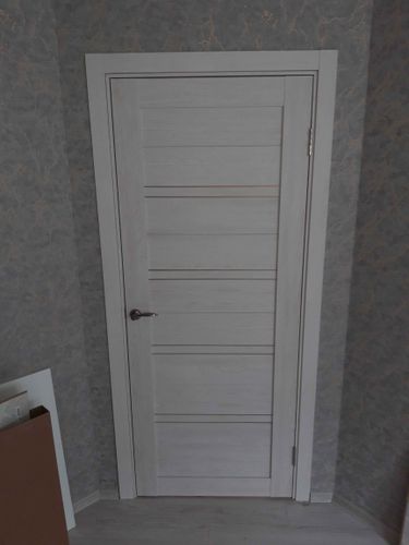 Установлена светлая одностворчатая дверь, закреплены петли, врезана ручка, отрегулированы зазоры, проверена плавность закрывания, завершена отделка наличниками.