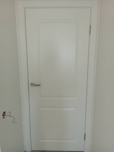 Установлена белая дверь с одной створкой, закреплены петли, врезана ручка. Полотно ровно встало в проем, обеспечивая плотное прилегание. Завершена отделка наличниками.