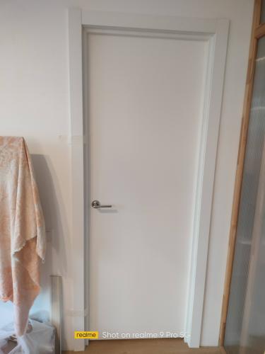 Установлена новая белая дверь с ручкой, аккуратно закреплена в проеме. Смонтированы наличники, обеспечивающие плотное прилегание. Работа завершена, все элементы на месте.