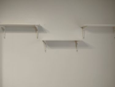 На стене закреплены три белые полки с помощью металлических уголков, обеспечивающих устойчивость и надежность конструкции.