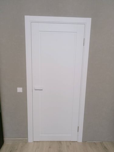 Установлена белая дверь с одной створкой, закреплены петли, врезана ручка, выровнена коробка, выполнена отделка наличниками, обеспечена плавная работа, завершена чистовая отделка.