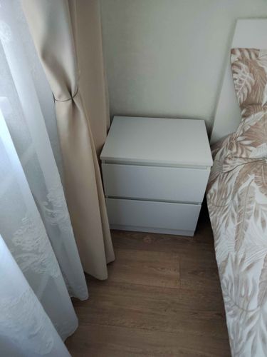 Собрана компактная мебель с двумя выдвижными ящиками, установлена рядом с кроватью. Белая поверхность гармонирует с интерьером, обеспечивая удобство хранения и стильный вид.