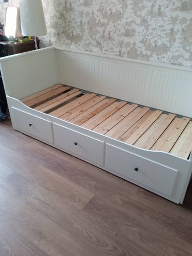 Собрана конструкция с деревянными ламелями и встроенными ящиками. Установлены боковые панели и задняя стенка. Все элементы надежно закреплены, обеспечивая устойчивость и функциональность.