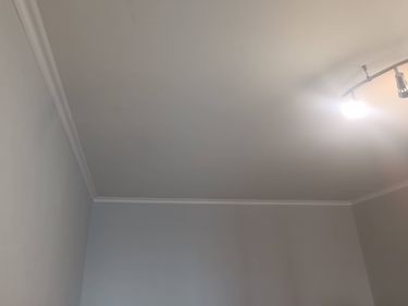 В комнате установлен потолочный плинтус, аккуратно закреплённый по периметру. Соединения ровные, без зазоров. Завершённый вид интерьера подчёркивает гармонию стен и потолка.