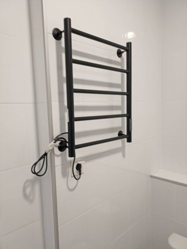 Электрический полотенцесушитель закреплён на стене, подключён к розетке. Все элементы установлены ровно, провод аккуратно уложен. Работа выполнена качественно и надежно.