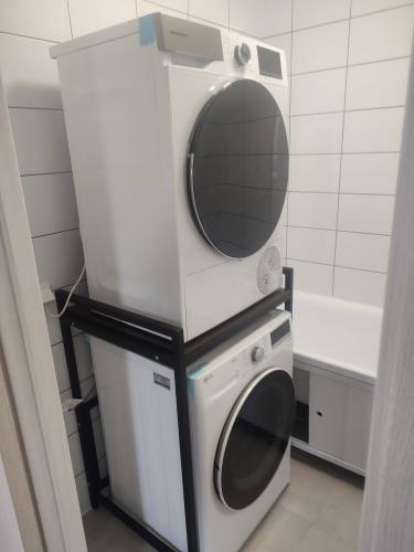 Изображена завершенная установка сушильного аппарата на стиральную машину с использованием специальной стойки. Подключение к электросети выполнено, обеспечена надежная фиксация и устойчивость конструкции.