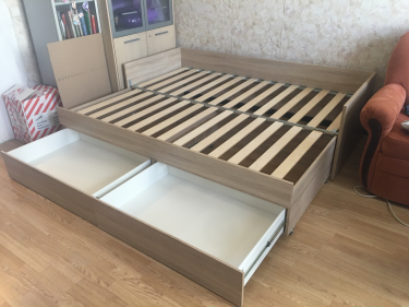 Собрана двуспальная кровать с выдвижными ящиками. Установлены боковые панели, закреплены ламели и направляющие. Все элементы соединены, конструкция устойчива и готова к использованию.