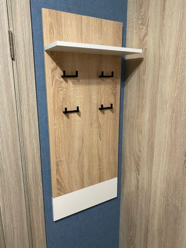 Закреплена деревянная панель на стене, установлены металлические крючки для одежды, добавлена верхняя полка для хранения. Компактная конструкция завершена, готова к использованию.