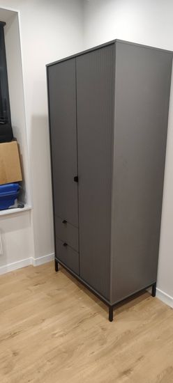 Собран шкаф с тремя ящиками и двумя дверцами. Установлен на ровный пол, обеспечена устойчивость. Все элементы надежно закреплены, конструкция завершена и готова к использованию.