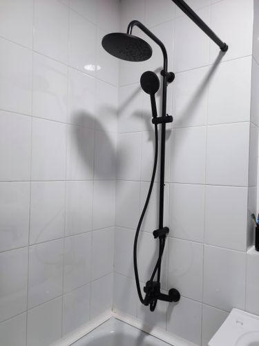 Выполнен монтаж нового душевого оборудования: установлены черные элементы, закреплены на стене, подключены к водопроводу, проверена герметичность соединений, обеспечена функциональность.