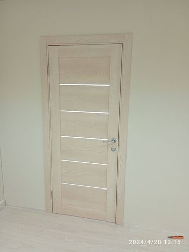 Установлена светлая дверь с ручкой и петлями, ровно закреплена в проеме, аккуратно подогнана под пол, обеспечивая плавное открывание и закрывание.