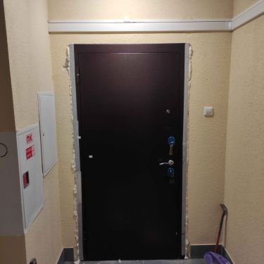 Изображена установленная металлическая дверь. Проем подготовлен, конструкция закреплена, зазоры заделаны монтажной пеной, установлены ручки и замки, завершена отделка откосов.