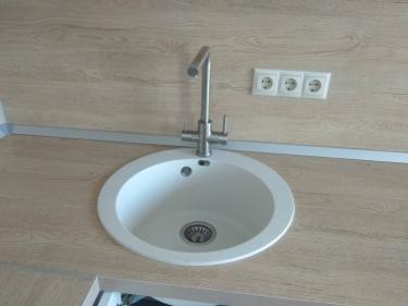 Изображение демонстрирует кухонную раковину после снятия водопроводного смесителя. Работы завершены, поверхность очищена, коммуникации отсоединены, место готово к установке нового оборудования.