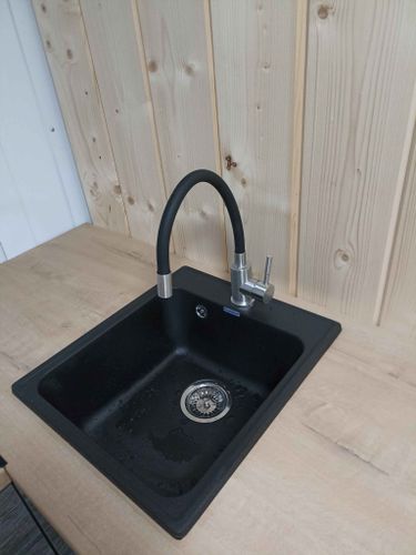 Установлена кухонная мойка с черной раковиной и смесителем на столешницу из древесно-стружечной плиты. Завершена подводка коммуникаций, обеспечена герметичность соединений.