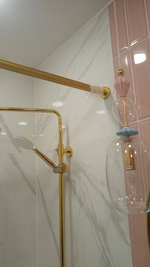 Закреплена металлическая штанга для душа золотистого оттенка на кафельной стене. Установлены крепления, обеспечивающие надежность и устойчивость конструкции.