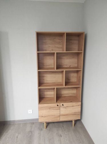 Собрано изделие из дерева: установлены полки, закреплены дверцы, прикручены ножки. Все элементы соединены, конструкция устойчива, готова к использованию.