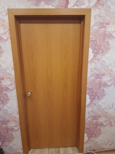 Установлена новая деревянная дверь с ручкой, закреплена в проеме, оформлена наличниками. Полотно ровно подогнано, зазоры отсутствуют, конструкция надежно зафиксирована, гармонично вписана в интерьер.