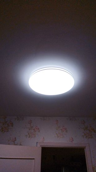 На потолке закреплено новое осветительное устройство с люминесцентными лампами, обеспечивающее яркое и равномерное освещение в помещении. Установка завершена, светильник функционирует.