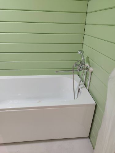 Изображение ванной комнаты с зеленой отделкой стен. Установлена новая ванна с современным смесителем, подключены водопроводные трубы. Все работы завершены аккуратно и качественно.