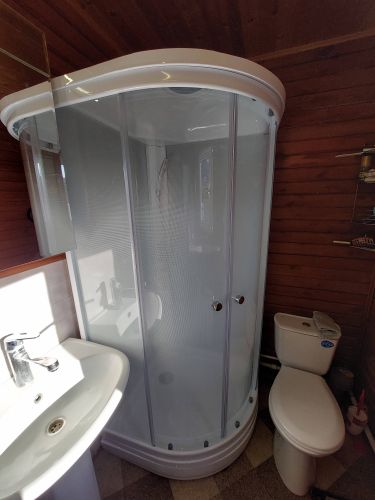 Изображение ванной комнаты с установленной душевой кабиной, раковиной и унитазом. Стены отделаны деревянными панелями, создавая уютную атмосферу.