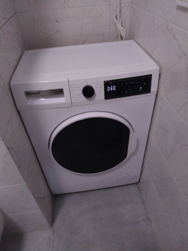 Изображение показывает установленную стиральную машину в углу ванной комнаты. Подключены водопровод и слив, устройство выровнено, проверена работа всех функций.