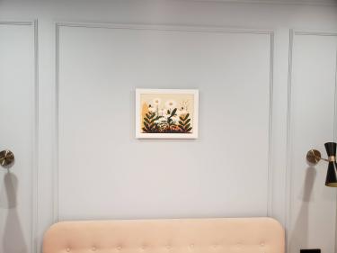 На стене закреплено изображение в рамке с цветочным мотивом. Композиция расположена симметрично, гармонирует с интерьером. Работа выполнена аккуратно, без видимых креплений.