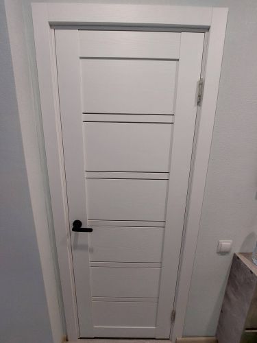 Установлена белая межкомнатная дверь с одной створкой, смонтированы петли, ручка и замок, выполнена подгонка полотна в проем, закреплены наличники, обеспечена плавная работа конструкции.