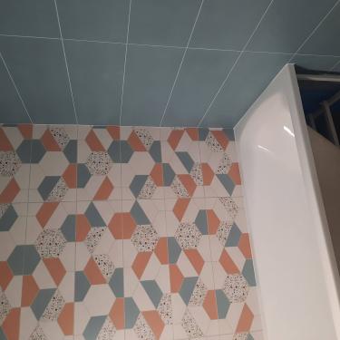 На стенах ванной комнаты уложен керамогранит с геометрическим узором и однотонными плитками. Завершенная работа демонстрирует аккуратное сочетание цветов и ровные швы.