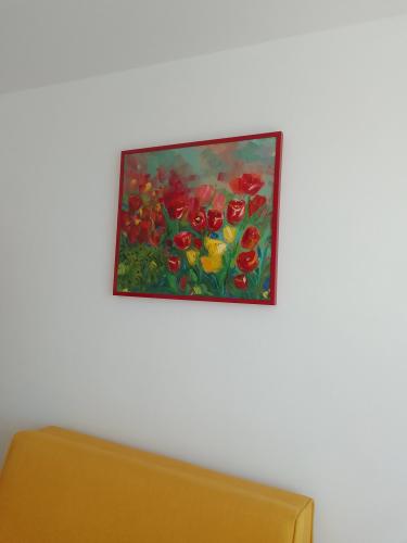Картина в яркой раме аккуратно закреплена на белой стене над жёлтым диваном, создавая гармоничную композицию и добавляя цветовой акцент в интерьер.