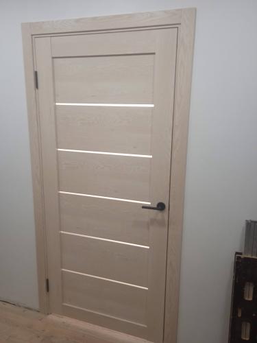 Установлена светлая деревянная дверь с горизонтальными вставками, закреплена на петлях, добавлена ручка. Полотно ровно вмонтировано в проем, обеспечивая плавное открывание и закрывание.