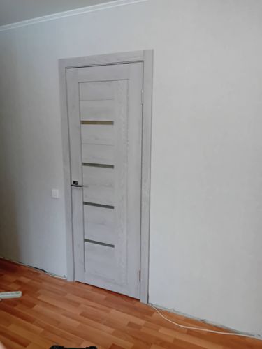 Установлена светлая дверь с ручкой и петлями, аккуратно закреплена в проеме, выровнена по уровню. Полотно плотно прилегает, обеспечивая плавное открывание и закрывание.